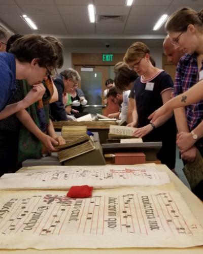 participants at a 2019 Cornell summer workshop on historical music notation examining medieval musical sources from the Kroch Library&#039;s Rare and Manuscript Collections
